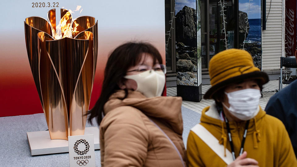 Seen here, locals in Tokyo pose next to the Olympic torch wearing face masks.