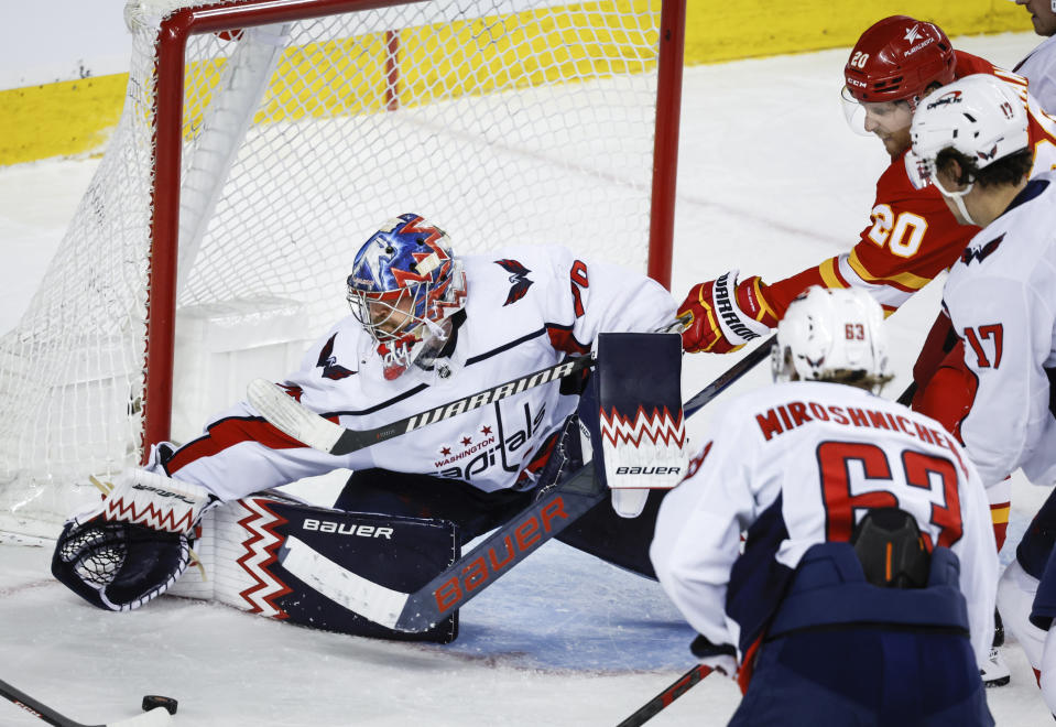 Washington Capitals goalie Charlie Lindgren, left, grabs for the puck as Calgary Flames forward Blake Coleman (20) tries to get his stick on it during the third period of an NHL hockey game in Calgary, Alberta, Monday, March 18, 2024. (Jeff McIntosh/The Canadian Press via AP)