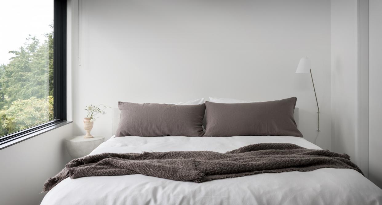  Close up image of the head of a bed with two grey rectangular cushions on white sheets. 