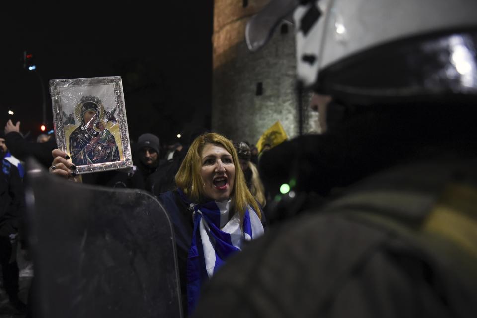 A woman holding a religious icon shouts slogans in front of riot police during a rally in the northern Greek city of Thessaloniki, Friday, Dec. 14, 2018. Hundreds of people protest against government efforts to end a three-decade-old dispute with neighboring Macedonia as the Greek Prime Minister Alexis Tsipras will deliver a speech to party cadres and supporters. (AP Photo/Giannis Papanikos)