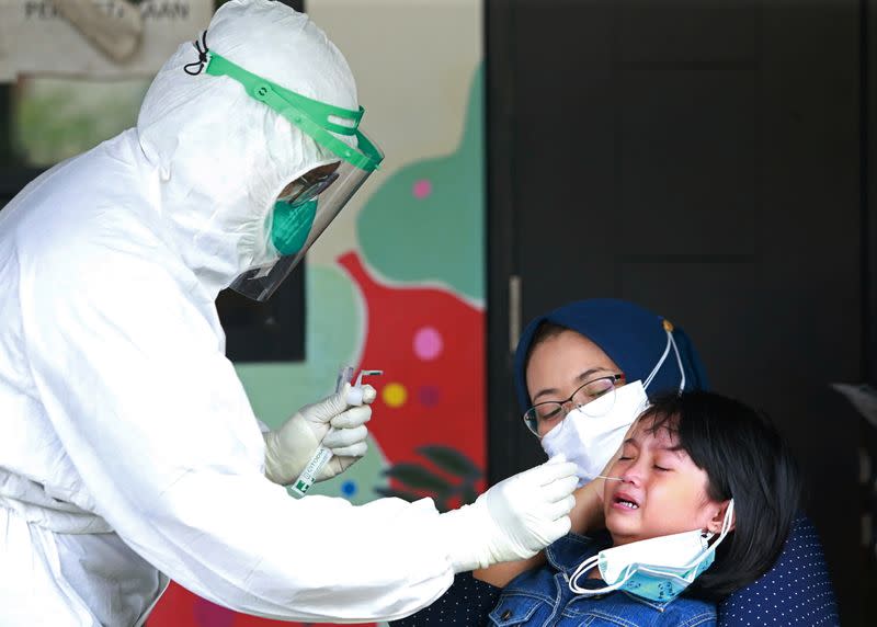A healthcare worker in personal protective equipment takes a swab sample from a young girl to test for the coronavirus disease (COVID-19) during mass testing at a school in Jakarta