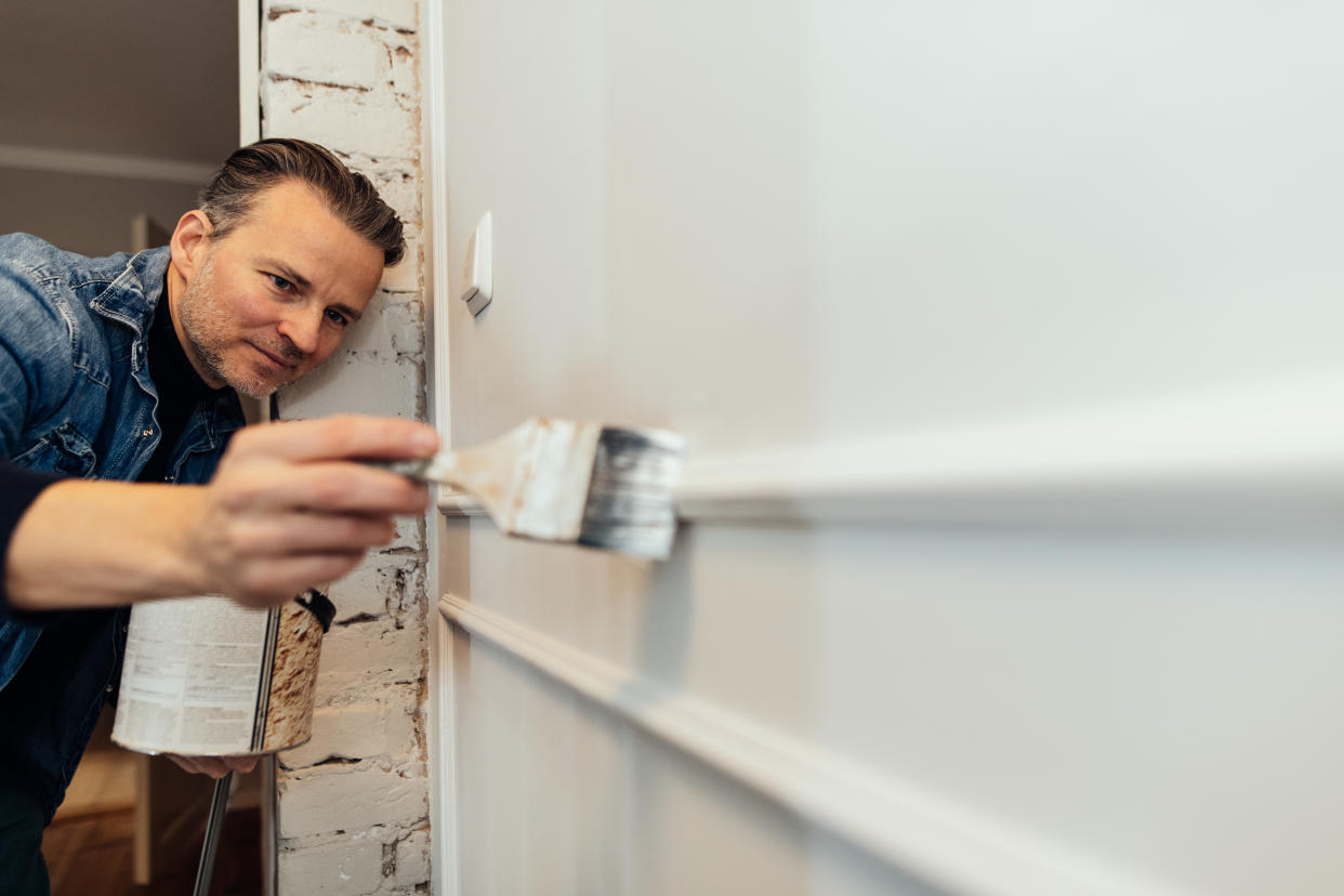 Man painting new decorative DIY wainscot panel at a wall in his house.