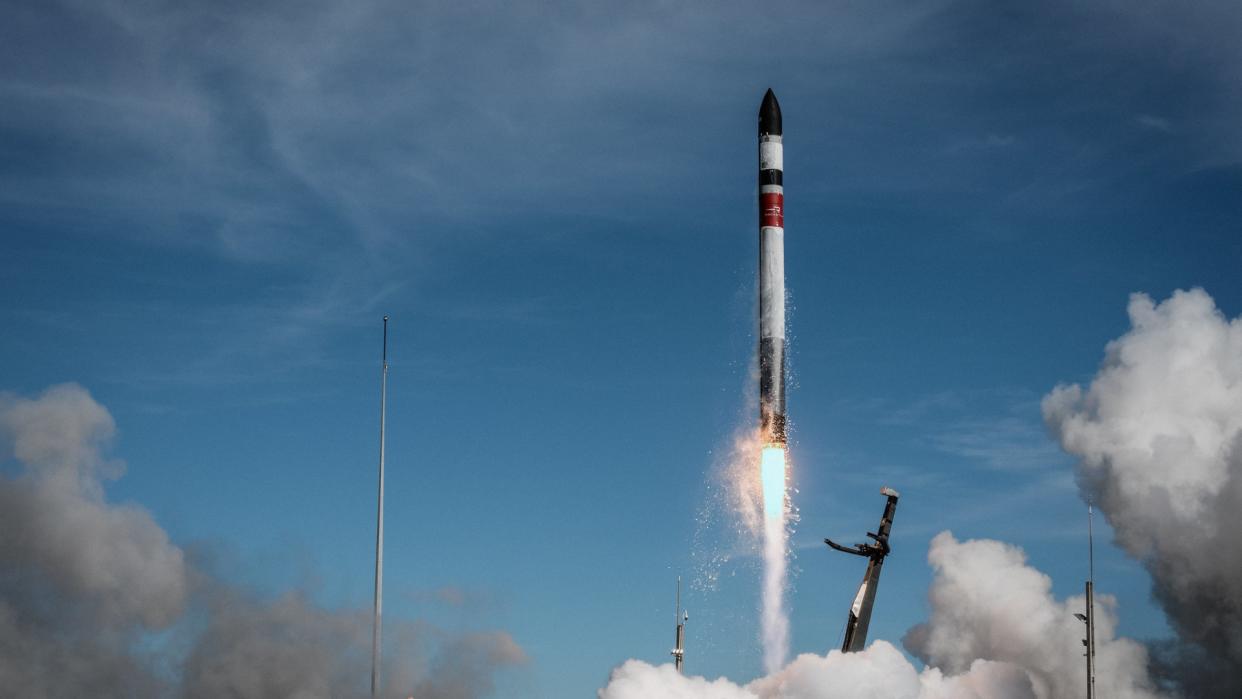  A black and white rocket lifts off under a sunny blue sky. 