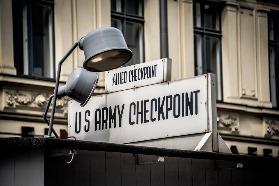 Sign reading "Allied Checkpoint" above and "U.S. Army Checkpoint" below on a building with a lamp overhead