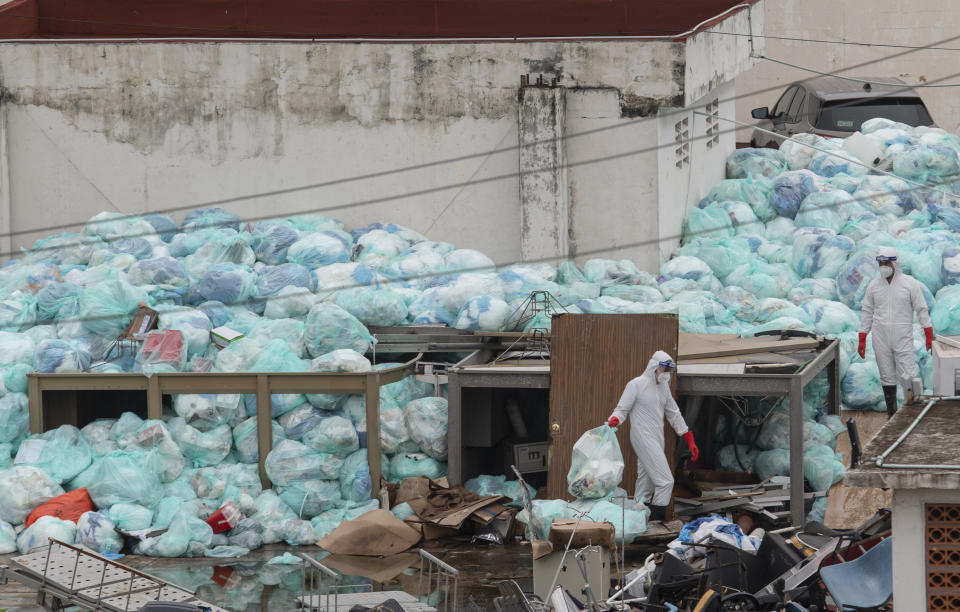 Medical workers using protective equipment dispose of trash bags containing hazardous biological waste into a large pile outside the Hospital del Instituto Mexicano del Seguro Social, which treats patients with COVID-19 in Veracruz, Mexico, Wednesday, Aug. 12, 2020. Improper disposal of medical waste has become an increasing problem in Mexico amid the pandemic. (AP Photo/Felix Marquez)