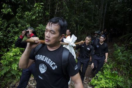 Members of a police forensic team carry a body bag with human remains dug from the grave near the abandoned human trafficking camp in the jungle close the Thailand border at Bukit Wang Burma in northern Malaysia May 27, 2015. REUTERS/Damir Sagolj