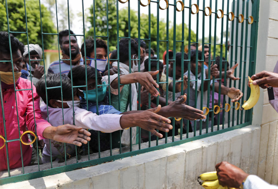 People who arrived from neighboring Madhya Pradesh state on Thursday stretch their hands out to receive a banana each before boarding a bus to be transported back to their native homes in Uttar Pradesh state in Prayagraj, India , Friday, May 1, 2020. The shelter-in-place orders imposed in India on March 24 halted all but essential services, sparking an exodus of migrant workers and people who survive on daily wages out of India's cities and toward villages in rural areas. Prime Minister Narendra Modi is due to announce on Sunday his decision whether to extend the 40-day-old lockdown or gradually ease it to resume economic activity. AP Photo/Rajesh Kumar Singh)