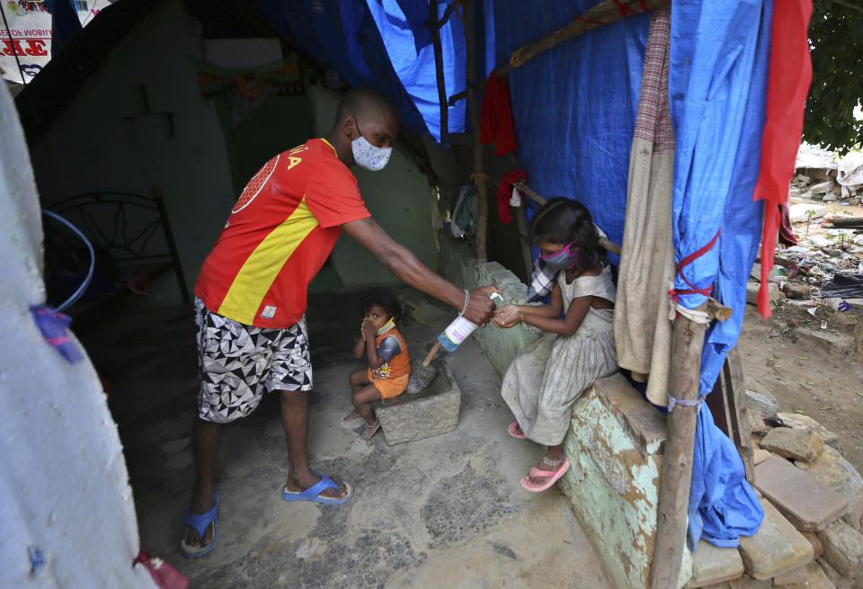 Gangaiah, son of Padmavathi who died of COVID-19, gives sanitizer to his elder daughter Shanti as two-year-old Priya looks on inside their family hut which is made from bamboo and plastic sheeting at a slum in Bengaluru, India, Thursday, May 20, 2021. Padmavathi collected hair, taking it from women's combs and hairbrushes to later be used for wigs. She earned about $50 a month. (AP Photo/Aijaz Rahi)