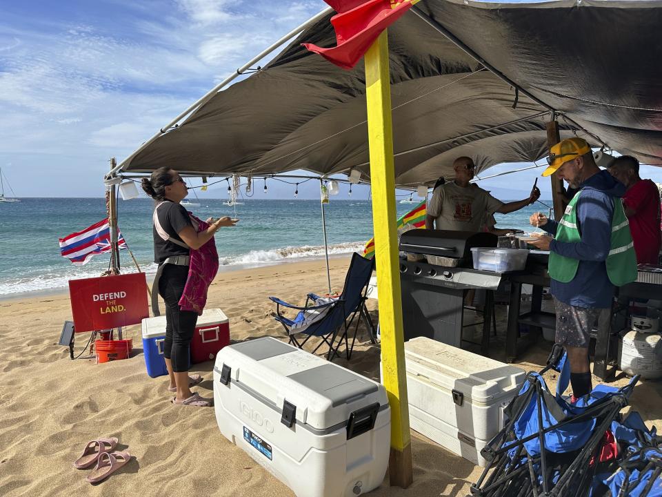 Jordan Ruidas, left, speaks to people at the Fishing for Housing camp on Kaanapali Beach in Lahaina, Hawaii on Wednesday, Nov.14, 2023. A group of Lahaina wildfire survivors is vowing to camp on a popular resort beach until the mayor uses his emergency powers to shut down unpermitted vacation rentals and make the properties available for residents in desperate need of housing. (AP Photo/Audrey McAvoy)
