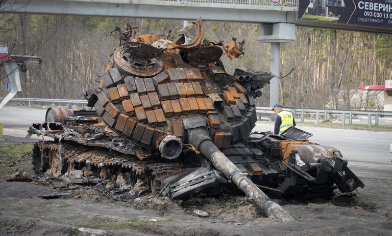 Un trabajador de la carretera examina un tanque ruso dañado en una carretera hacia Kiev, Ucrania