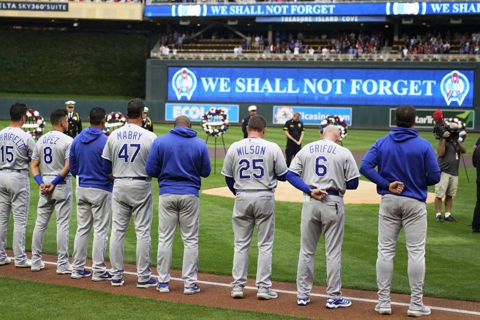 A moment of silence is observed by the Kansas City Royals baseball players as wreathes stood behind the mound to mark the 20th anniversary of Sept. 11, 2001 prior to the Royals at Minnesota game, Saturday, Sept. 11, 2021, in Minneapolis. (AP Photo/Jim Mone)