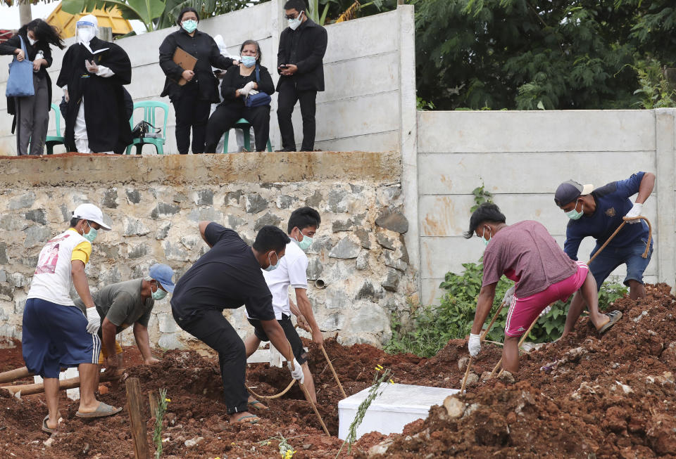 Workers bury a man as family members watch in the special section of the Jombang cemetery opened to accommodate the surge in deaths during coronavirus outbreak in Tangerang, Indonesia, Tuesday, Jan. 26, 2021. Indonesia has reported more cases of the virus than any other countries in Southeast Asia. (AP Photo/Tatan Syuflana)