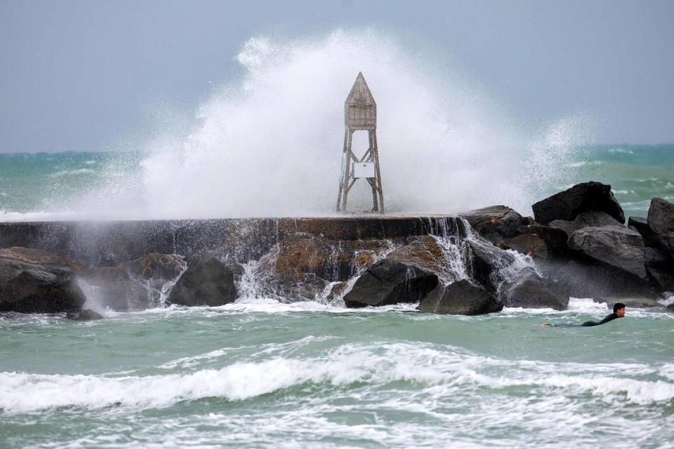 A surfer takes advantage of the weather by the Bal Harbour Lighthouse as the waves crash against the jetty on Thursday, Dec. 14, 2023 in Bal Harbour, Fla. The gusty winds, heavy rain, flooded streets and other hazards are expected continue over the weekend in Miami, Fort Lauderdale and Palm Beach.