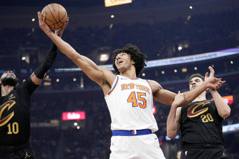 New York Knicks center Jericho Sims (45) reaches for a rebound between Cleveland Cavaliers guard Darius Garland (10) and forward Georges Niang (20) in the first half of an NBA basketball game, Sunday, March 3, 2024, in Cleveland. (AP Photo/Sue Ogrocki)