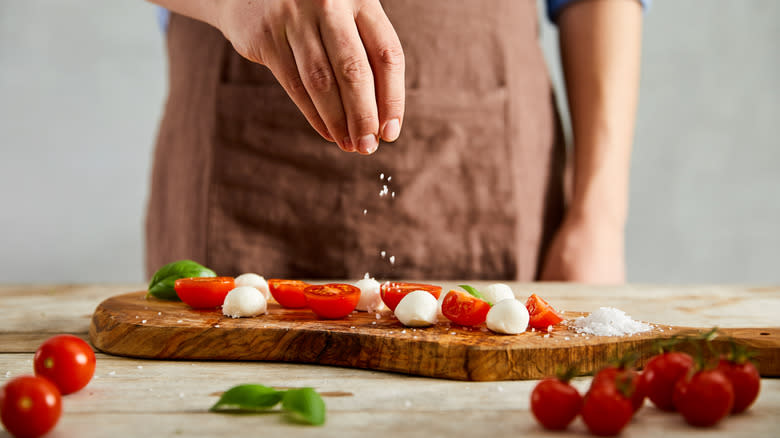 Person sprinkling salt on tomatoes