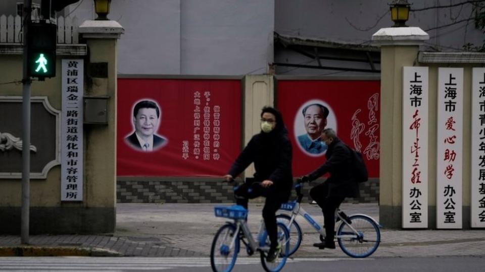 Gente con mascarillas pasando al lado de retratos de Xi Jinping y de Mao Zedong.