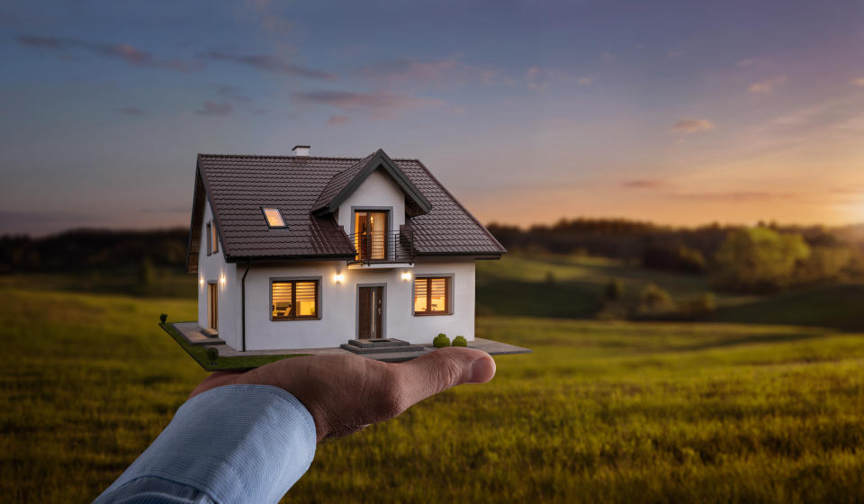 Male hand holding a new dream house at an empty field.