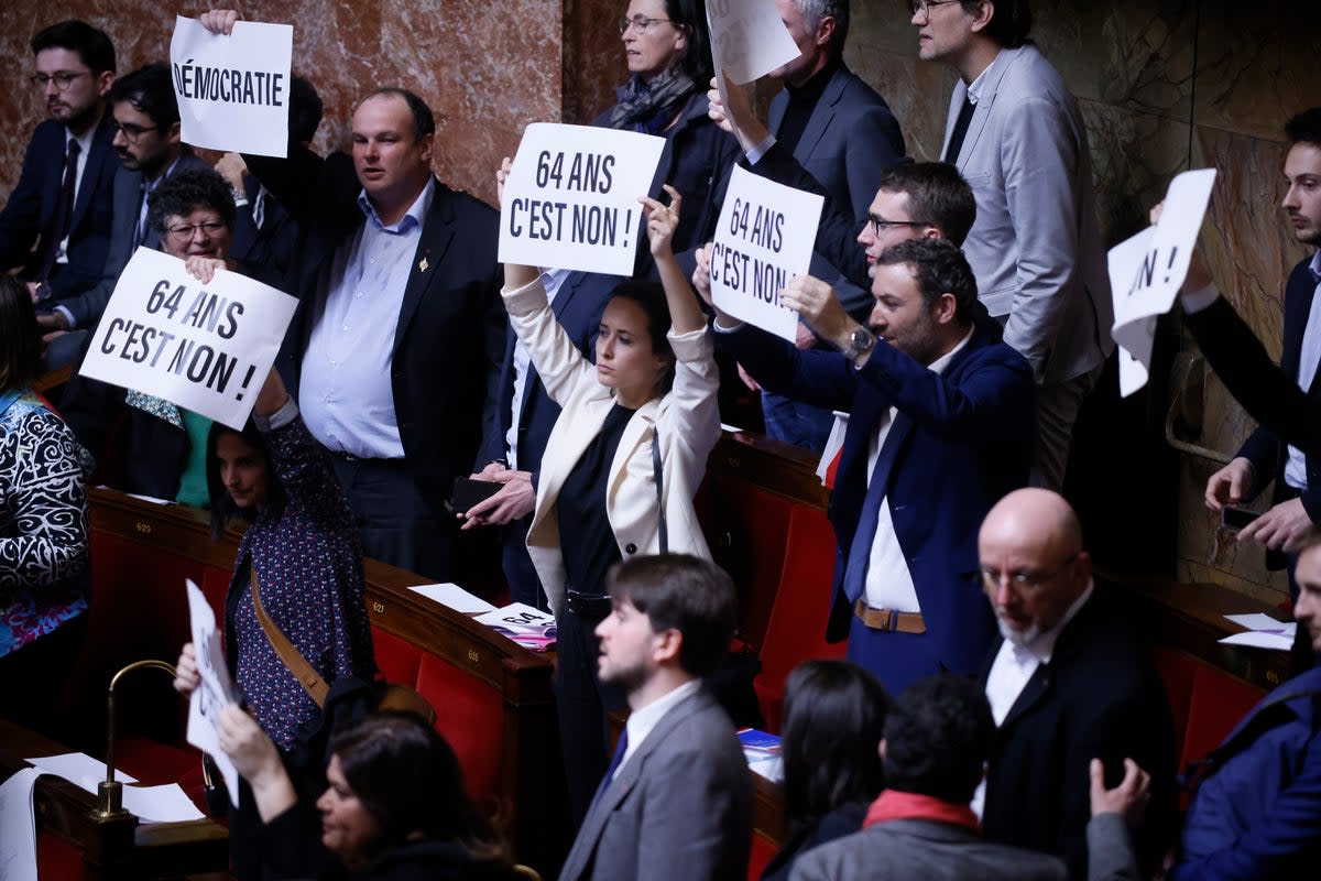 Far-left legislators react as they hold papers reading: ‘64 years. It is no’ at the National Assembly in Paris (AP)