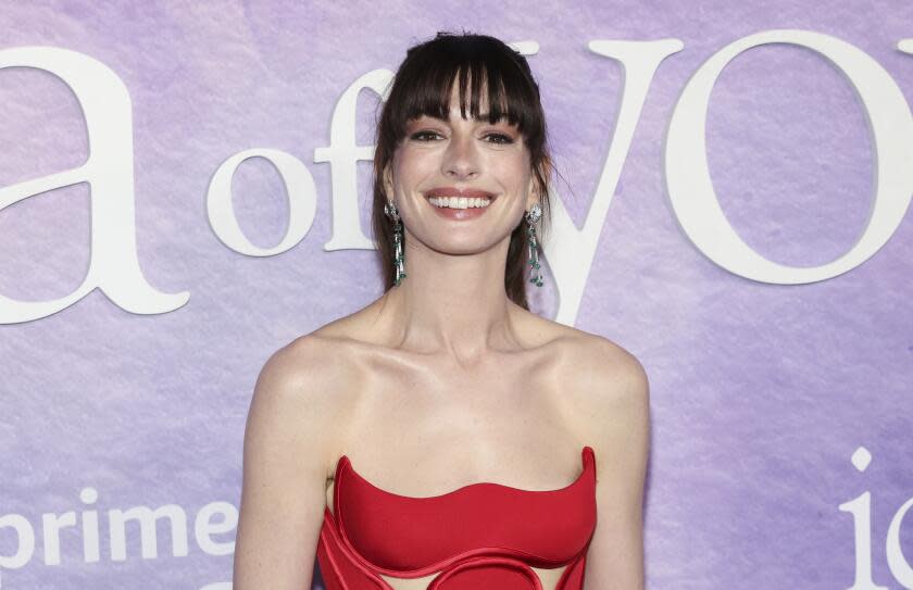 Anne Hathaway smiling in a strapless red dress and dangly earrings with her long dark hair pulled back from her face
