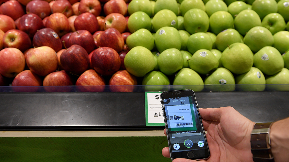 Green and red apples on a shelf in Woolworths as a man holds up a Scan&Go phone app.