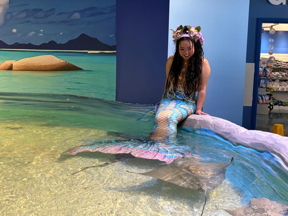 Mermaid Nixie sits on the edge of a pool that houses sharks and sting rays during an event at Blue Zoo in West Des Moines on May 11, 2024.