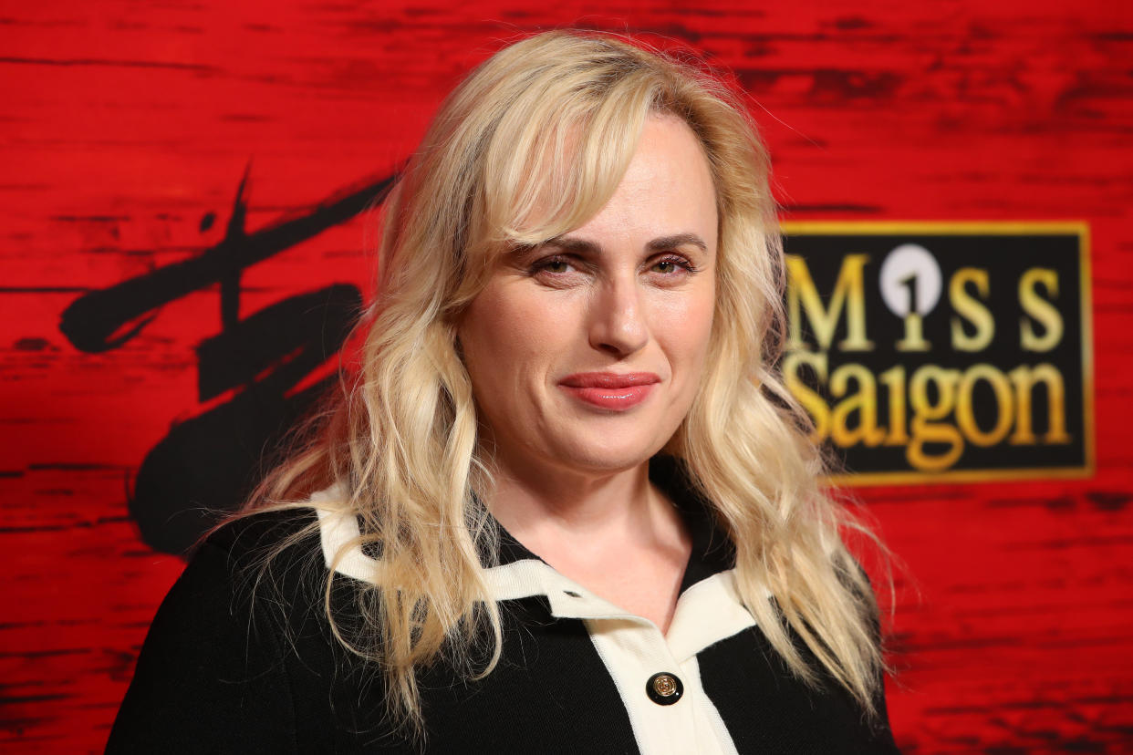 Rebel Wilson photographed in front of a red background with the words Miss Saigon.