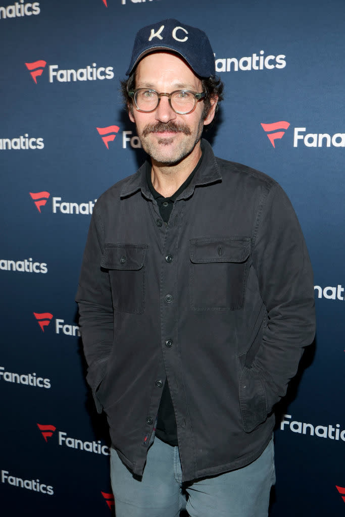 Man in cap and glasses poses with hands in pockets at Fanatics event