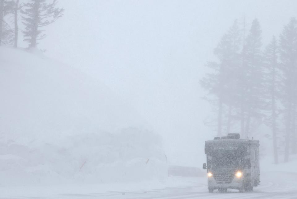 A vehicle drives past a snowbank as snow falls in the Sierra Nevada mountains on March 28, 2023, in Mammoth Lakes, California.