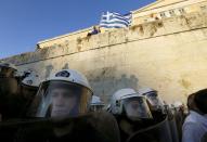 A protester waves a Greek flag as riot policemen stand guard at the parliament building during a rally calling on the government to clinch a deal with its international creditors and secure Greece's future in the Eurozone, in Athens, Greece, June 22, 2015. REUTERS/Yannis Behrakis