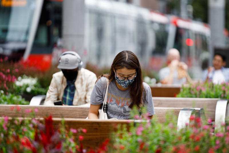 A woman seated on a public bench wears a face mask while reading a book in Sydney.