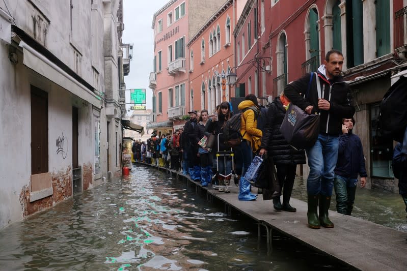 People walk on a catwalk in the flooded street during a period of seasonal high water in Venice