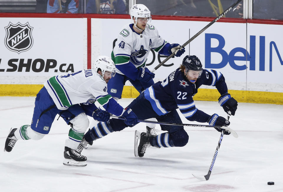 Winnipeg Jets' Mason Appleton (22) reaches out for the pass as Vancouver Canucks' Conor Garland (8) and Elias Pettersson (40) defend during the third period of an NHL hockey game Thursday, April 18, 2024, in Winnipeg, Manitoba. (John Woods/The Canadian Press via AP)