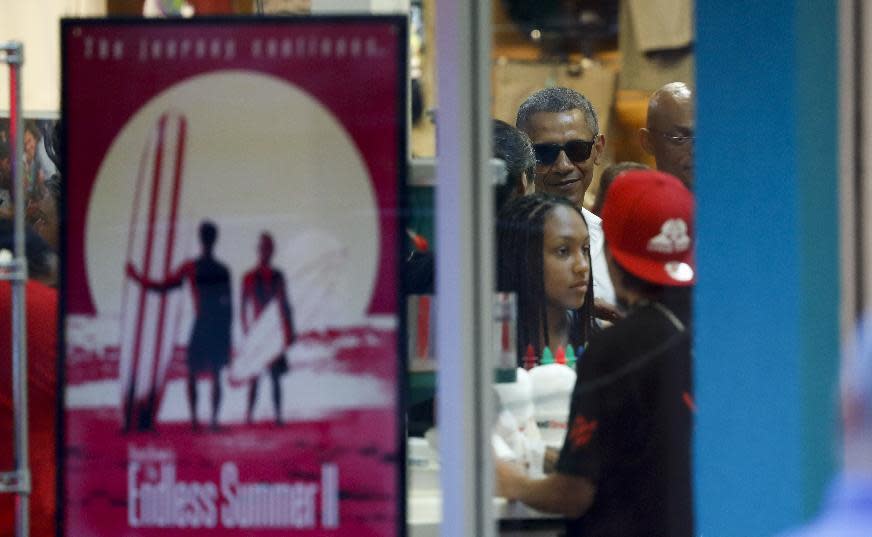 President Barack Obama, wearing sunglasses, is seen through the window of Island Snow Hawaii as he and family and friends order shave ice in Kailua, Hawaii, Saturday, Dec. 24, 2016, during the first family's annual vacation. (AP Photo/Carolyn Kaster)