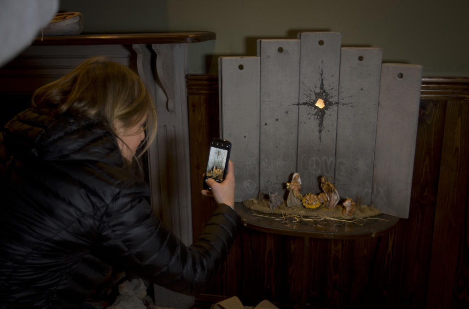 A Christian visitor takes pictures of a new artwork dubbed "Scar of Bethlehem" by the artist Banksy displayed in The Walled Off Hotel, in the West Bank city of Bethlehem, Sunday, Dec. 22, 2019. (AP Photo/Majdi Mohammed)