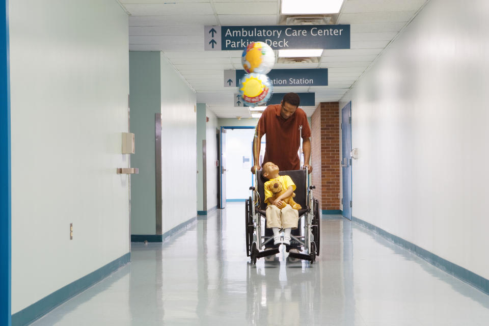 African father pushing son in wheelchair down hospital corridor