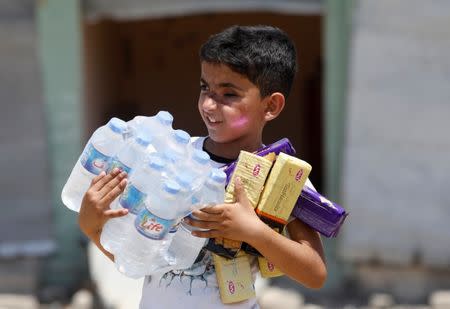 A boy carries bottles of water and biscuits given by an aid organization during the first day of Eid-al Fitr celebration in West Mosul, Iraq June 25, 2017. REUTERS/Erik De Castro