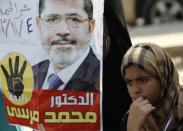 A supporter of the Muslim Brotherhood and ousted Egyptian President Mohamed Mursi stands next to a poster of Mursi during a protest outside the police academy, where Mursi's trial took place, on the outskirts of Cairo, November 4, 2013. Mursi struck a defiant tone on the first day of his trial on Monday, chanting 'Down with military rule', and calling himself the country's only 'legitimate' president. Mursi, an Islamist who was toppled by the army in July after mass protests against him, appeared angry and interrupted the session repeatedly, prompting a judge to adjourn the case. The words on the poster read, "Mursi is our president." REUTERS/Amr Abdallah Dalsh (EGYPT - Tags: POLITICS CIVIL UNREST)