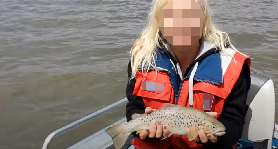 A woman with a blurred face holding a trout on a lake in Tasmania.