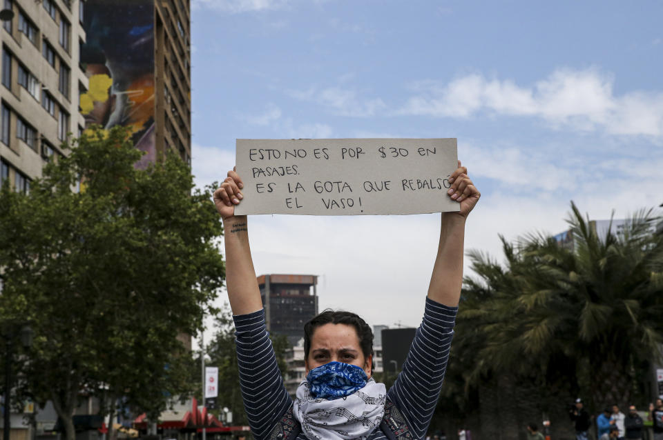 A demonstrator raises a sign that reads in Spanish "This is not for 30 pesos in fare, it's the drop that overflows the glass" during a protest in Santiago, Chile, Saturday, Oct. 19, 2019. The protests started on Friday afternoon when high school students flooded subway stations, jumping turnstiles, dodging fares and vandalizing stations as part of protests against a fare hike, but by nightfall had extended throughout Santiago with students setting up barricades and fires at the entrances to subway stations, forcing President Sebastian Pinera to announce a state of emergency and deploy the armed forces into the streets. (AP Photo/Esteban Felix)