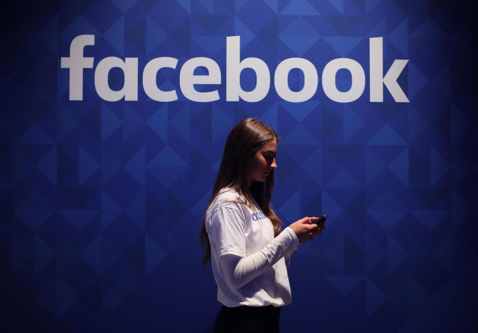 File photo dated 03/11/15 of a woman using her phone under a logo of Facebook. The prevalence of hate speech on Facebook is decreasing, the social media giant has claimed, as it published its latest report on how the site enforces its rules. The firm said hate speech was now appearing in around five posts per 10,000, down from between five and six per 10,000 in the first three months of this year. Issue date: Wednesday August 18, 2021.