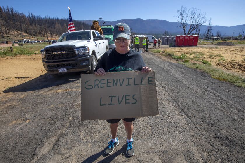 Greenville, CA - July 16: Cathy Buchanan, 46, holds a handmade cardboard "Greenville Lives" sign at the start of the Greenville's Gold Diggers Day parade route on Saturday, July 16, 2022, in Greenville, CA. A year ago, the Dixie fire tore through this tiny Plumas County town, decimating all but a few homes and businesses. (Francine Orr / Los Angeles Times)