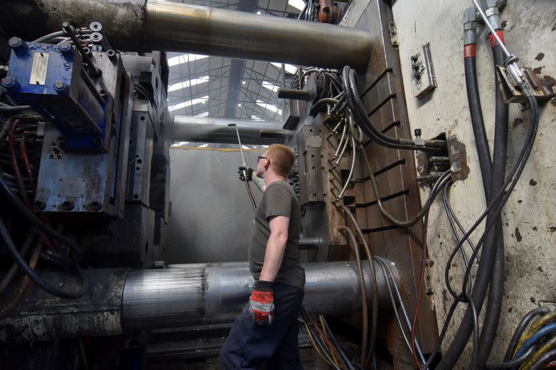 A worker at Evtec Aluminium Ltd sprays an aluminium casting machine with water between uses at the company's foundry, in Kidderminster