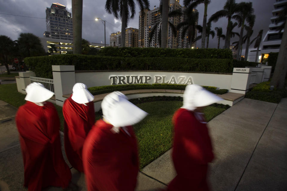 Demonstrators dressed as characters from the Hulu show "The Handmaid's Tale," based on the Margaret Atwood novel of the same name, walk past signage for Trump Plaza during a protest in West Palm Beach, Florida, on Nov. 11, 2017.