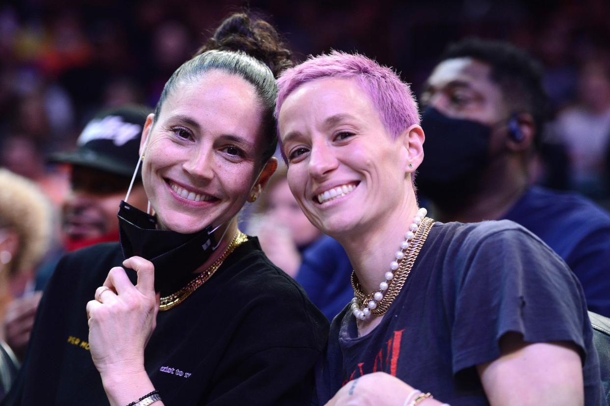 Sue Bird (left) and Megan Rapinoe pose from the sidelines of an NBA game.