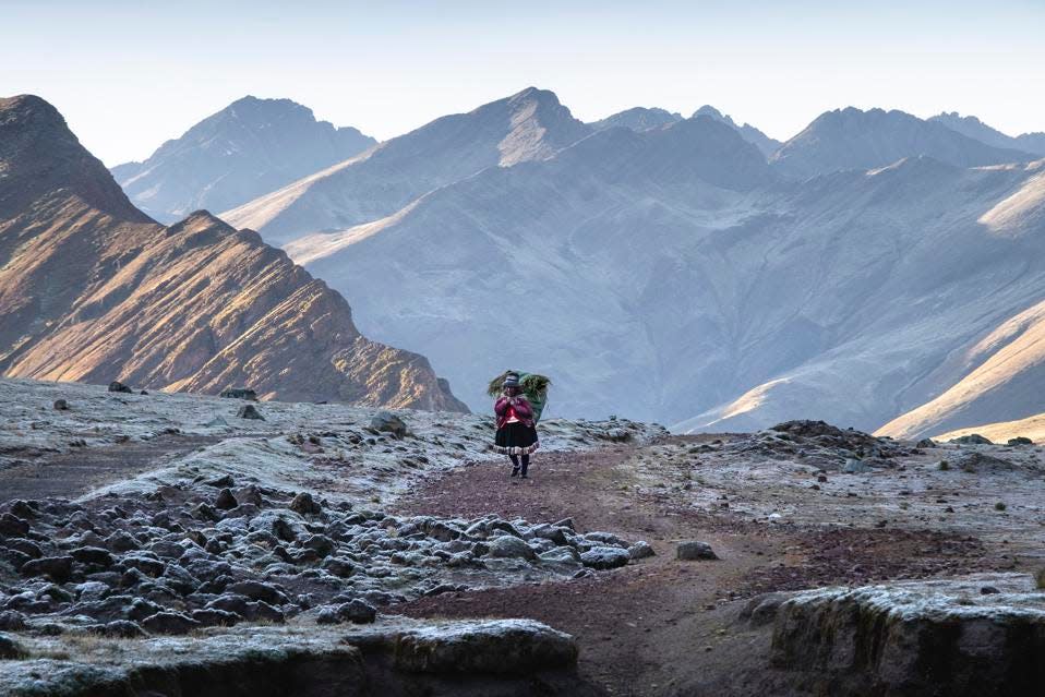 Una mujer solitaria que lleva una gran carga caminando por la cordillera andina peruana.