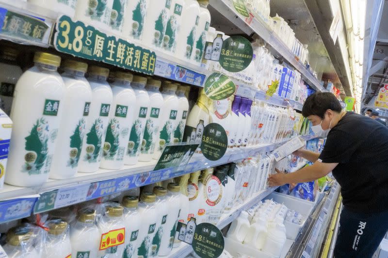 Staff member places cartons of milk on refrigerator shelves at a supermarket in Beijing