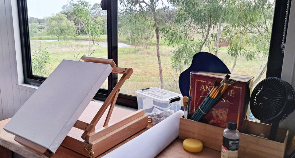 An easel set up in front of a window overlooking the countryside from inside a tiny home.  