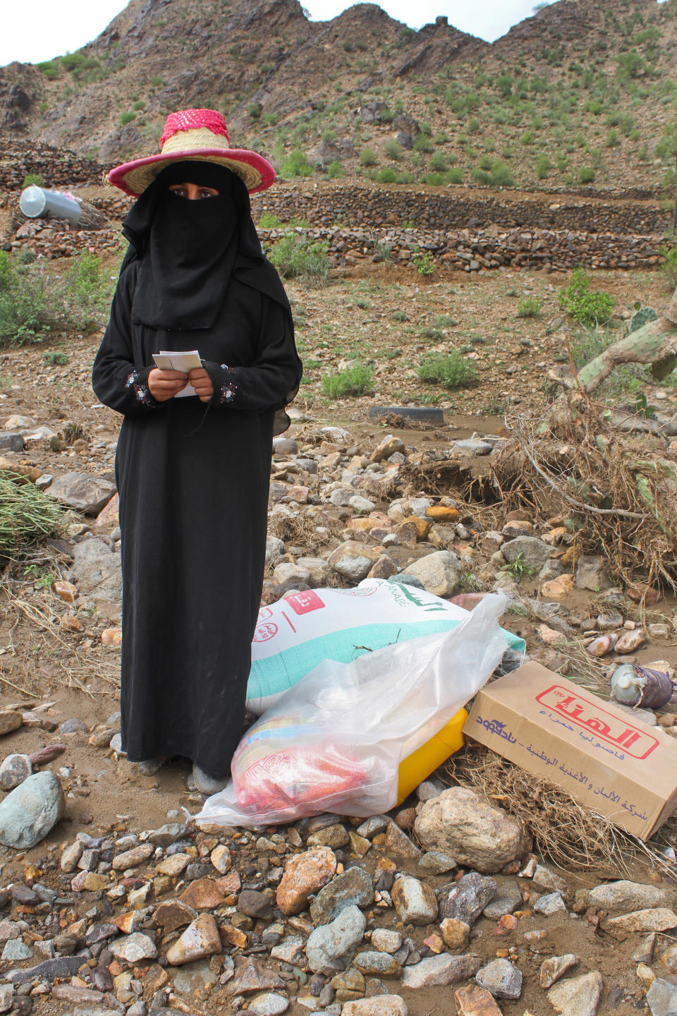 A woman stands with her monthly ration of food items provided by Mercy Corps.&nbsp;
