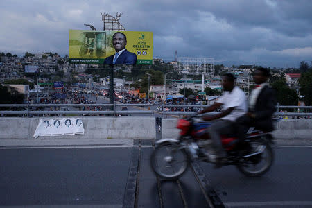 Men riding a motorbike pass an electoral billboard of presidential candidate Jude Celestin of LAPEH (Alternative League for Progress and Emancipation of Haiti) party, ahead of the presidential election, in a street of Port-au-Prince, Haiti, November 17, 2016. REUTERS/Andres Martinez Casares