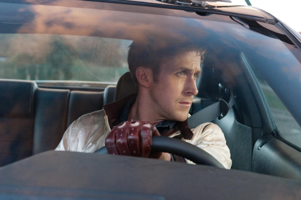 Ryan Gosling stares out the driver's side window of a car while wearing driving gloves